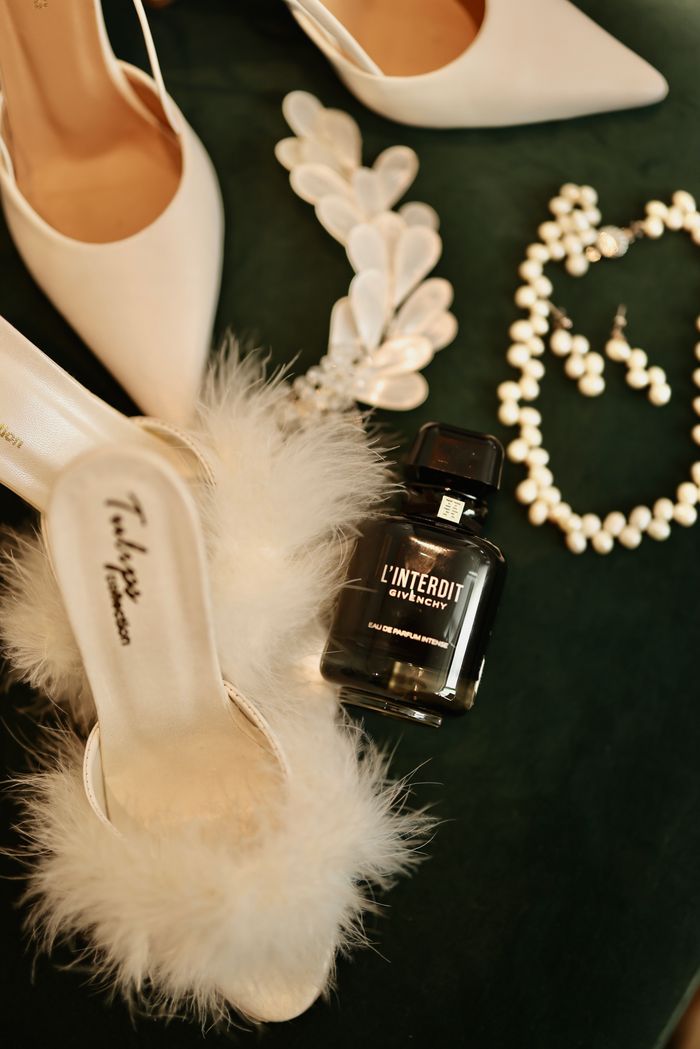about-img Flat lay of elegant wedding shoes, jewelry, and perfume on a dark background.