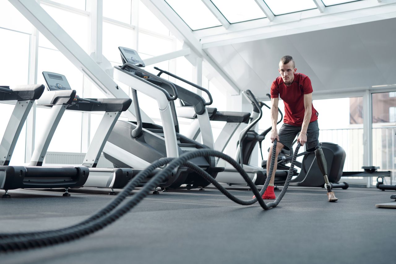 Crafting Captivating Headlines: Your awesome post title goes here Young man with prosthetic leg working out in a modern gym with battle ropes, showcasing strength and determination.