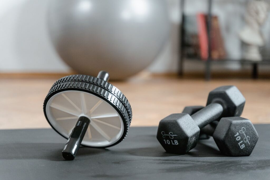 pexels photo 8032833 Close-up of ab wheel and dumbbells on a mat in a home gym setting.