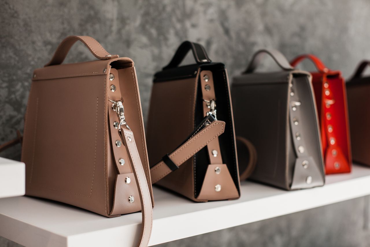 services-03 Luxury leather handbags displayed on a white shelf, showcasing minimalistic design and various colors.